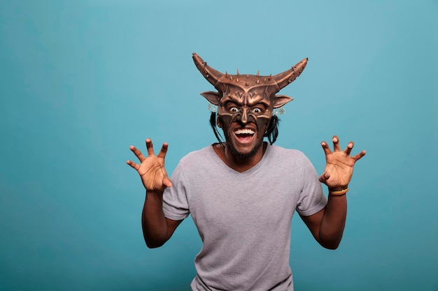 Young person wearing traditional indigenous face mask used in shaman culture and history to create native tribal ritual. Man using traditional tribe art and cultural object for entertainment.