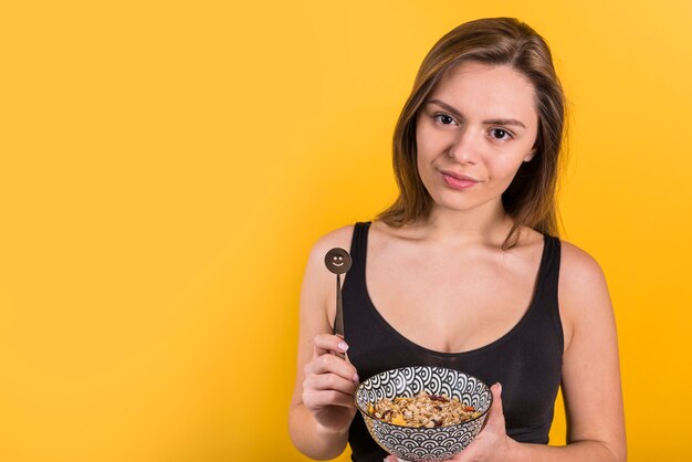 Young positive woman with chocolate spoon and bowl of flakes