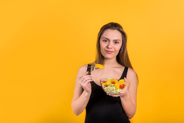 Young positive woman with fork and bowl of salad