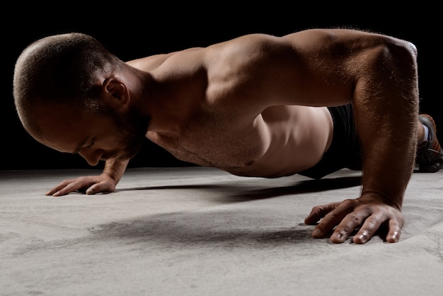 Free photo young powerful sportsman training push ups over dark wall.