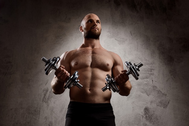 Free photo young powerful sportsman training with dumbbells over dark wall.