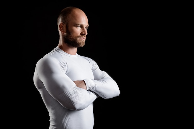 Young powerful sportsman in white clothing over black wall.