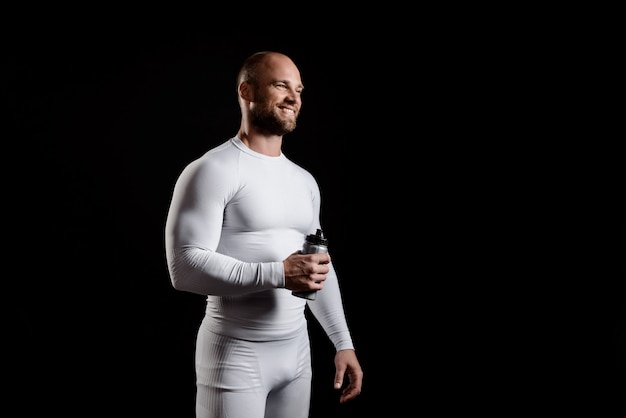 Young powerful sportsman in white clothing over black wall.