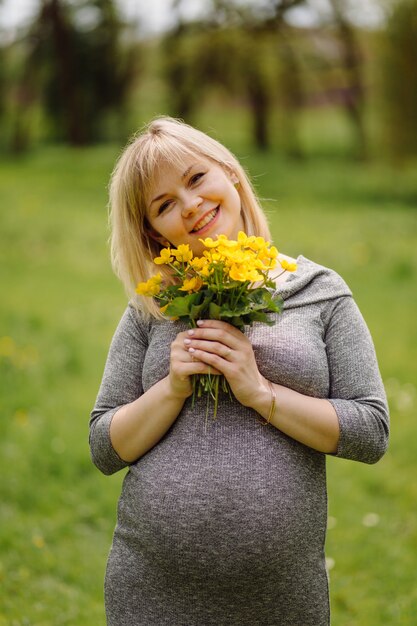 Young pregnant blonde woman in grey dress, pregnant girl in spring on a walk, maternity concept