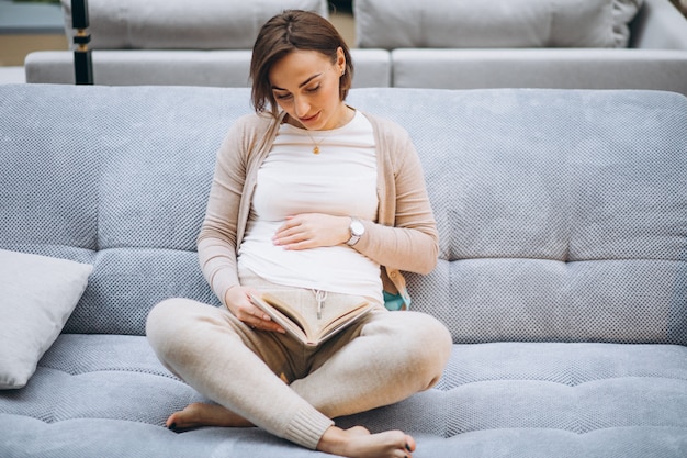 Young pregnant woman reading a book at home