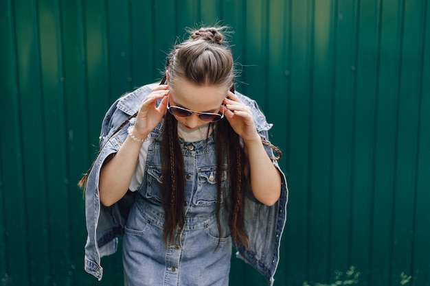 Young pretty attractive girl in denim clothes in glasses on a simple dark green background with empty place for text