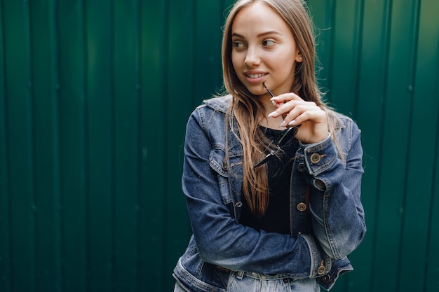 Young pretty attractive girl in denim clothes in glasses on a simple dark green background with empty place for text