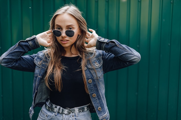 Young pretty attractive girl in denim clothes in glasses on a simple dark green background with empty place for text