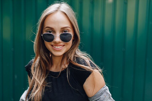 Young pretty attractive girl in denim clothes in glasses on a simple dark green wall with place for text.