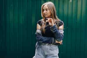 Free photo young pretty attractive girl in denim clothes in glasses on a simple dark green wall with place for text.