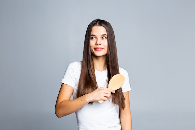 Young pretty brunette woman combing her beautiful long hair on white