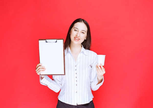 Free Photo young pretty businesswoman posing with empty clipboard and plastic cup. 