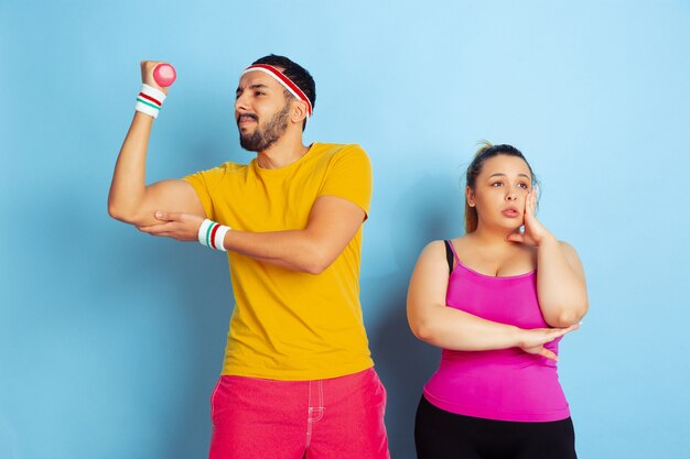 Young pretty caucasian couple in bright clothes training on blue space Concept of sport, human emotions, expression, healthy lifestyle, relation, family