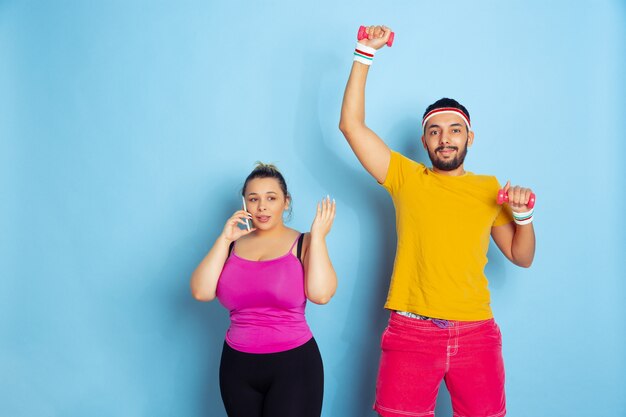 Young pretty caucasian couple in bright clothes training on blue space Concept of sport, human emotions, expression, healthy lifestyle, relation, family