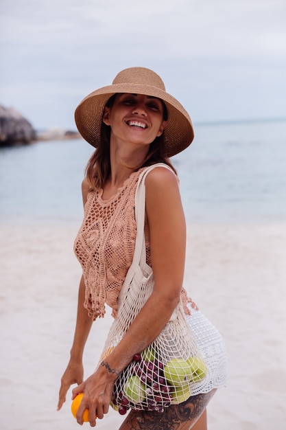 Young pretty caucasian tanned fit woman in knitted clothes and hat on beach