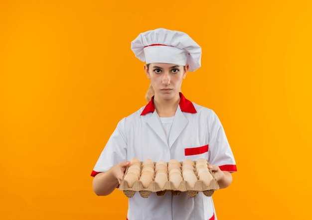 Young pretty cook in chef uniform holding carton of eggs