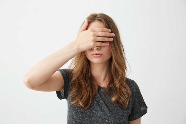 Young pretty girl covering closing eyes behind hand .