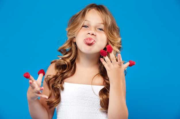 Young pretty girl eating raspberry over blue wall