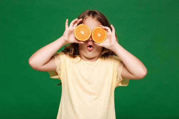 Young pretty girl hiding eyes with oranges over green wall