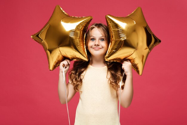 Young pretty girl holding baloons and smiling over pink wall