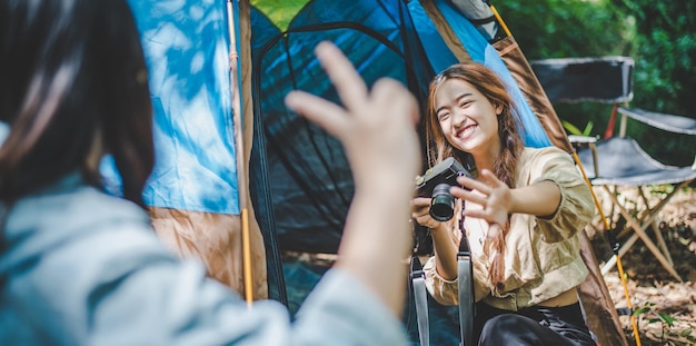 Young pretty photography herfriend by digital camera while sitting at the camping tent in forest Young Asian group women travel outdoor camping