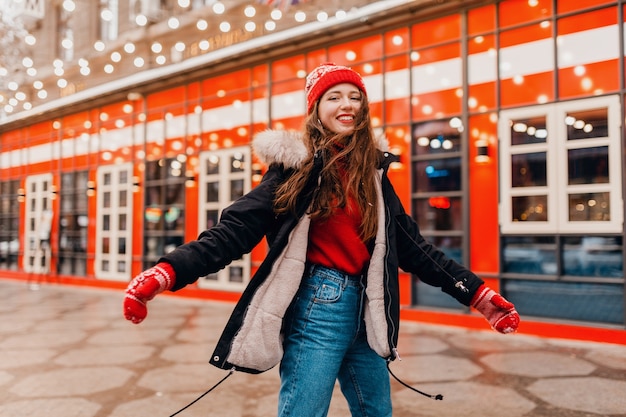 Free photo young pretty smiling happy woman in red mittens and knitted hat wearing winter coat walking in city christmas street, warm clothes style fashion trend