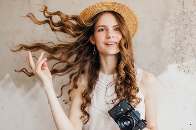 Young pretty smiling happy woman wearing white blouse sitting against wall in straw hat