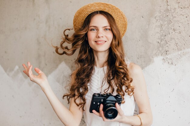 Young pretty smiling happy woman wearing white blouse sitting against wall in straw hat