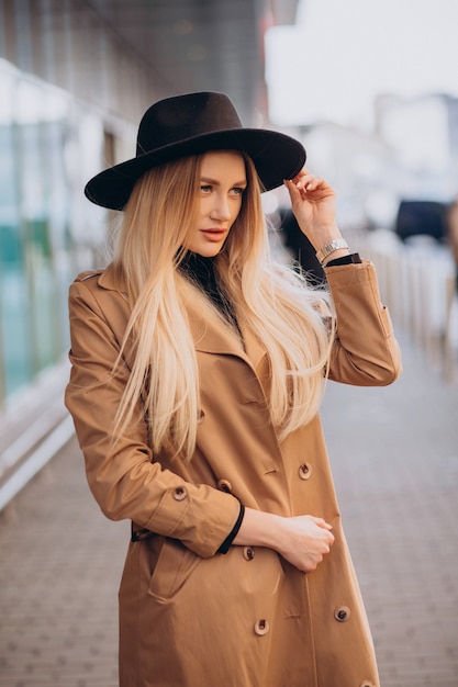 Free Photo young pretty woman in black hat and beige coat walking by mall