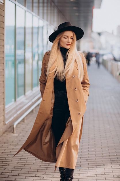 Free photo young pretty woman in black hat and beige coat walking by mall