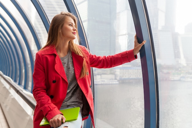 Young pretty woman in casual outfit holding tablet laptop in urban building