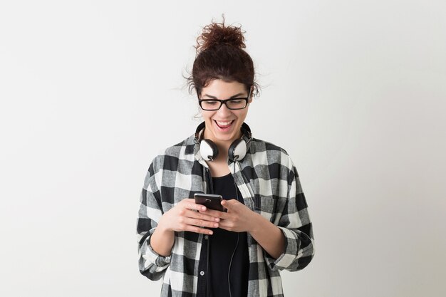 Free Photo young pretty woman in glasses, using smartphone, surprised face expression, funny emotion, laughing, positive, happy, headphones, isolated, checkered shirt, hipster style, student, typing message