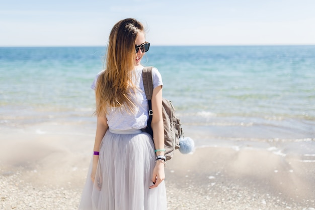 Young pretty woman in gray T-shirt and lush skirt is standing near sea