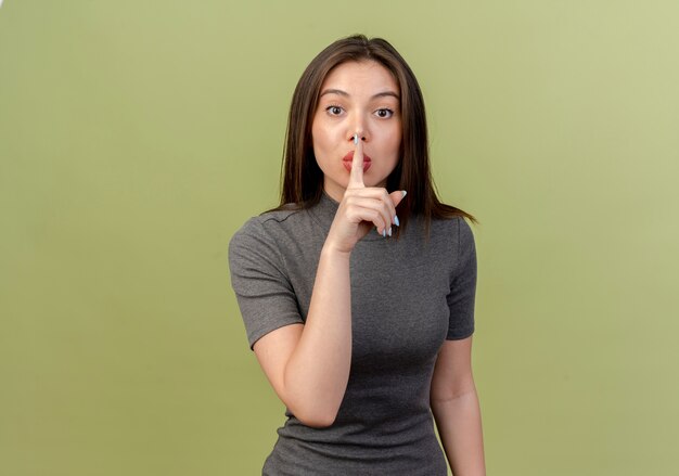 Young pretty woman looking at camera and doing silence gesture isolated on olive green background with copy space