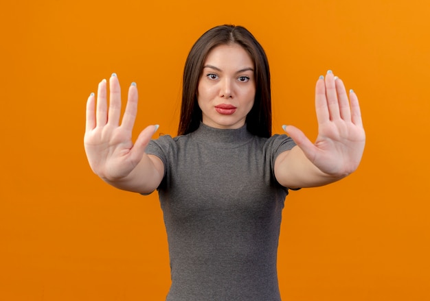 Young pretty woman looking at camera and gesturing stop isolated on orange background