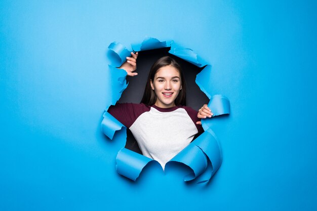 Young pretty woman looking through blue hole in paper wall.