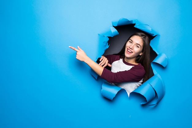 Young pretty woman pointed side while looking through blue hole in paper wall.