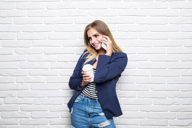 Young pretty woman speak on phone over white brick wall