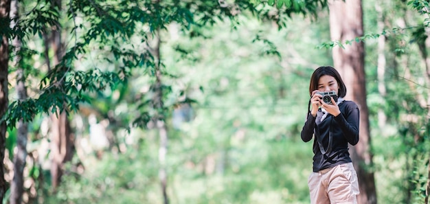 Young pretty woman use digital camera taking a photo beautiful nature while camping in forest with happiness copy space