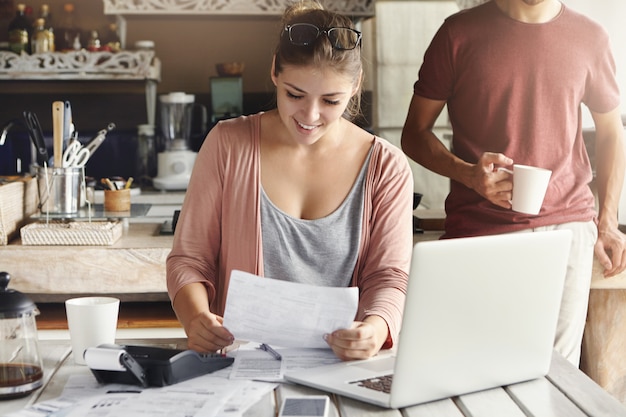 Young pretty woman wearing glasses on her head smiling happily while reading document saying that bank approved their mortgage application