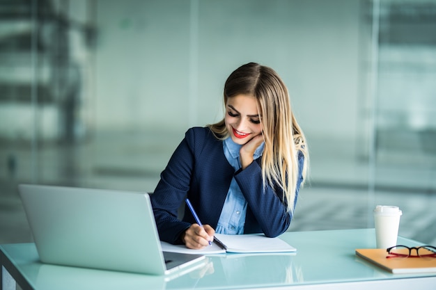 Young pretty woman working with laptop and taking notes on a desktop at Office