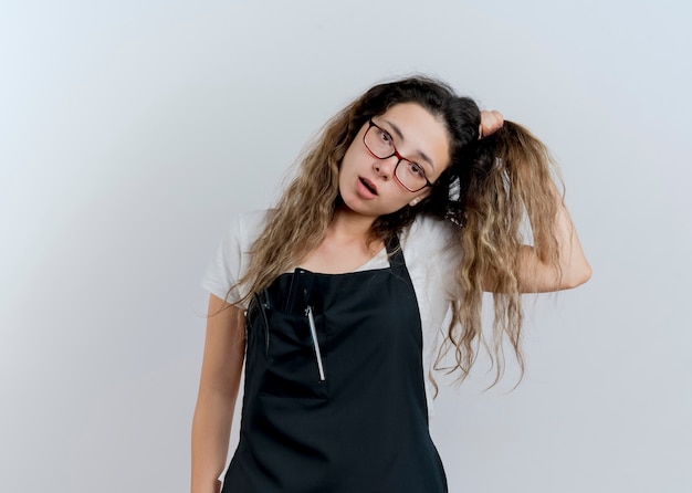 Free photo young professional hairdresser woman in apron confused touching her hair