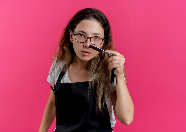 Young professional hairdresser woman in apron holding razor with serious expression 