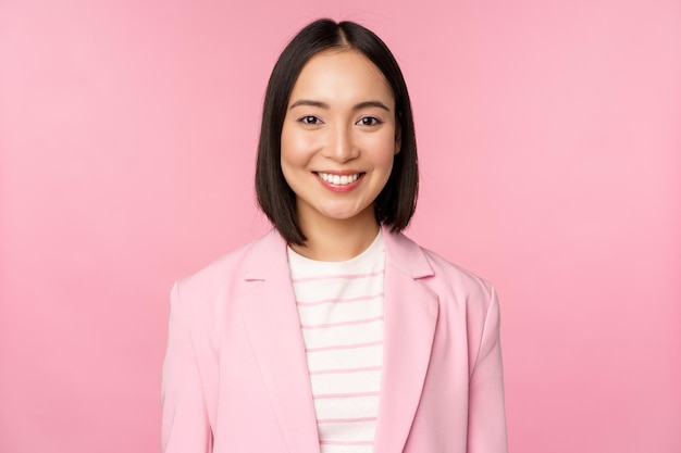 Young professionals Smiling asian businesswoman saleswoman in suit looking confident at camera posing against pink background