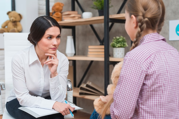 Free photo young psychologist observing little girl sitting in front of her