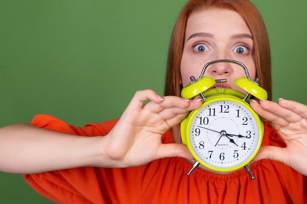 Free Photo young red hair woman in casual orange blouse on green wall holding alarm clock sleepy tired exhausted