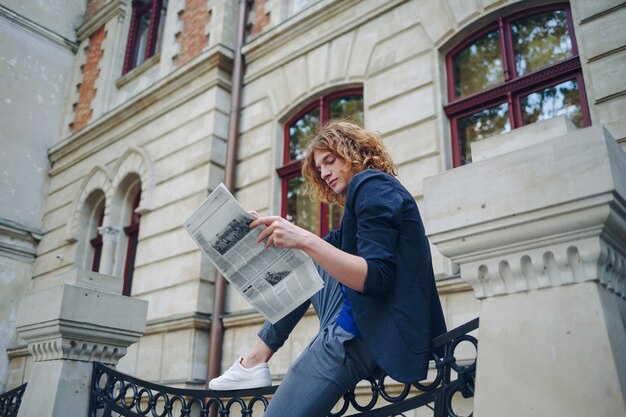 Young reddish man reading newspaper near old style building