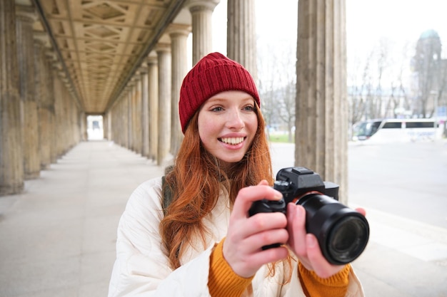 Free photo young redhead female photographer makes lifestyle shooting in city centre takes photos and smiles lo