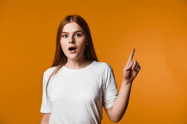 Young redhead girl has surprised look and is pointinting one finger aside up