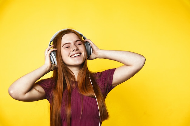 Young redhead girl is happy and listening music via headphones with closed eyes